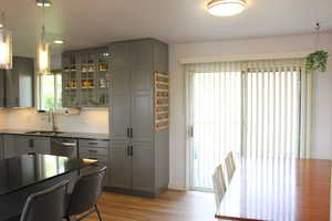 Kitchen with decorative light fixtures, dishwasher, sink, gray cabinetry, and light hardwood / wood-style floors