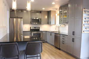 Kitchen with appliances with stainless steel finishes, decorative light fixtures, sink, a breakfast bar area, and gray cabinetry