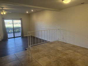 Empty room with a textured ceiling, dark tile patterned floors, ceiling fan, brick wall, and beam ceiling