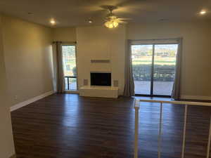 Unfurnished living room featuring dark wood-type flooring, ceiling fan, and a fireplace