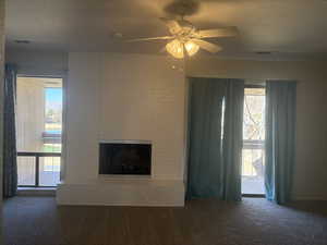 Unfurnished living room featuring ceiling fan, a fireplace, a textured ceiling, and dark colored carpet