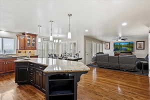 Kitchen with light stone counters, sink, a kitchen island with sink, and dark wood-type flooring