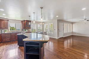Kitchen featuring dark wood-style floors, a kitchen island with sink, light stone countertops, decorative backsplash, and recessed lighting