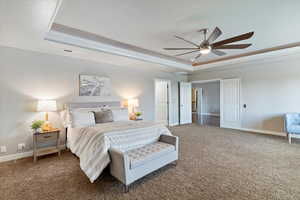 Carpeted bedroom with a tray ceiling, ornamental molding, and a ceiling fan