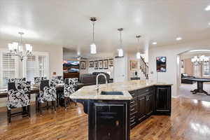 Kitchen featuring sink, wine cooler, hanging light fixtures, a kitchen island with sink, and light stone counters