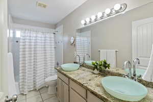 Bathroom featuring shower / tub combo with curtain, light tile patterned floors, and double vanity