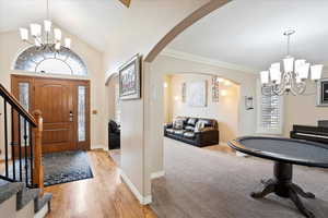 Foyer entrance with lofted ceiling, crown molding, light hardwood / wood-style flooring, and a chandelier