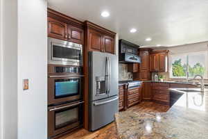 Kitchen featuring stainless steel appliances, dark wood-type flooring, light stone counters, backsplash, and recessed lighting