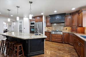 Kitchen featuring sink, a breakfast bar area, hanging light fixtures, an island with sink, and stainless steel appliances