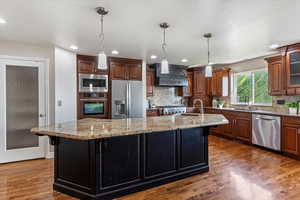 Kitchen featuring dark wood-type flooring, light stone countertops, hanging light fixtures, stainless steel appliances, and backsplash
