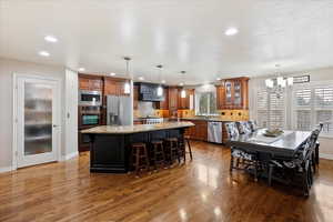 Kitchen with appliances with stainless steel finishes, a breakfast bar, tasteful backsplash, light stone countertops, and a center island with sink