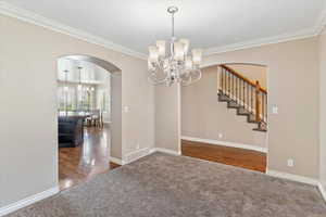 Unfurnished dining area with a chandelier, arched walkways, dark carpet, ornamental molding, and dark wood-type flooring