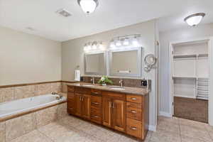 Full bathroom with double vanity, light tile patterned flooring, a bath, and a spacious closet