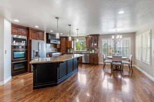 Kitchen featuring tasteful backsplash, dark stone counters, a chandelier, appliances with stainless steel finishes, and a center island with sink