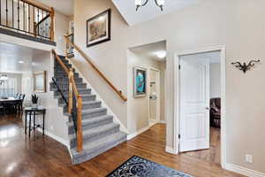 Staircase with a towering ceiling, wood-type flooring, and a chandelier