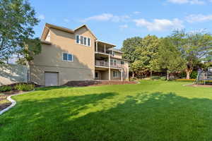 Rear view of house with stucco siding, a lawn, a trampoline, and a balcony