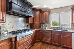 Kitchen featuring backsplash, premium range hood, dark wood-style flooring, dark stone countertops, and stainless steel gas stovetop