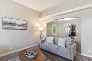 Carpeted living area with a chandelier, arched walkways, and ornamental molding