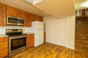 Kitchen featuring tasteful backsplash, dark wood-type flooring, light stone countertops, and appliances with stainless steel finishes