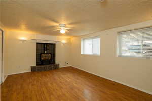 Unfurnished living room featuring wood-type flooring, a wood stove, a textured ceiling, and ceiling fan