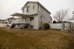 Rear view of property featuring central AC unit, a deck, and a lawn