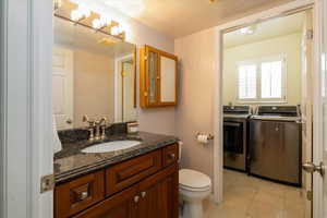 Bathroom with tile patterned flooring, vanity, independent washer and dryer, and toilet