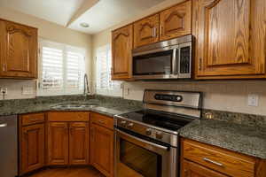 Kitchen with tasteful backsplash, sink, stainless steel appliances, and dark stone counters