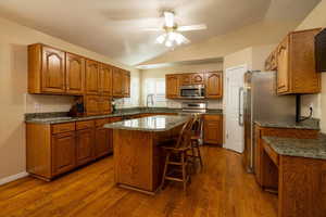 Kitchen featuring vaulted ceiling, appliances with stainless steel finishes, dark hardwood / wood-style floors, a kitchen breakfast bar, and a center island