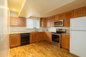 Kitchen with tasteful backsplash, sink, stainless steel appliances, light stone countertops, and light wood-type flooring