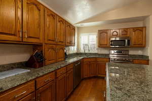 Kitchen with lofted ceiling, sink, appliances with stainless steel finishes, dark stone countertops, and hardwood / wood-style floors