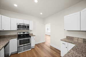 Kitchen with stainless steel appliances, white cabinetry, dark stone countertops, and light hardwood / wood-style floors