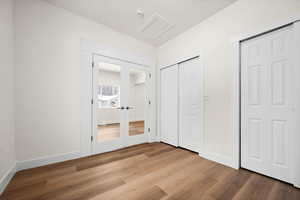 Unfurnished bedroom with hardwood / wood-style flooring, multiple closets, and french doors