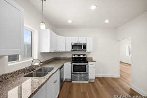 Kitchen with sink, decorative light fixtures, appliances with stainless steel finishes, stone counters, and white cabinets