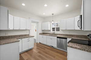 Kitchen with appliances with stainless steel finishes, pendant lighting, sink, white cabinets, and light hardwood / wood-style flooring