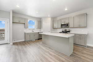 Kitchen featuring sink, light wood-type flooring, appliances with stainless steel finishes, gray cabinets, and a kitchen island