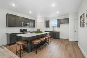 Kitchen featuring a breakfast bar, sink, light wood-type flooring, a kitchen island, and stainless steel appliances