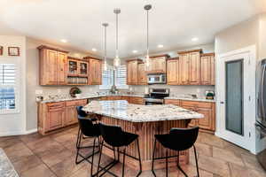 Kitchen with a kitchen bar, granite countertops, decorative light fixtures, appliances with stainless steel finishes, a kitchen island, and a wealth of natural light