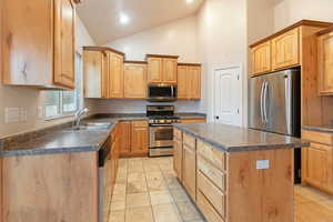 Kitchen with sink, light tile patterned floors, appliances with stainless steel finishes, high vaulted ceiling, and a center island