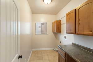 Laundry room with light tile patterned flooring, cabinets, a textured ceiling, washer hookup, and hookup for an electric dryer