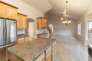 Kitchen featuring light tile patterned floors, stainless steel fridge, a kitchen island, a notable chandelier, and pendant lighting