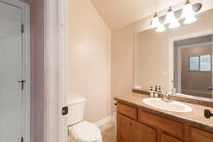 Bathroom featuring vanity, tile patterned floors, toilet, and lofted ceiling