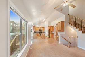 Unfurnished living room with ceiling fan, light carpet, and high vaulted ceiling