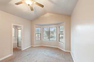 Empty room with ceiling fan, vaulted ceiling, and light carpet