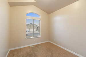 Carpeted empty room featuring vaulted ceiling