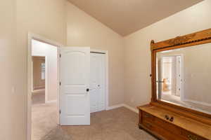 Unfurnished bedroom featuring vaulted ceiling, light colored carpet, and a closet