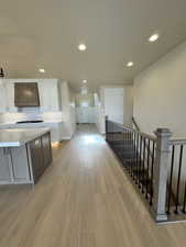 Kitchen with white cabinets, decorative backsplash, a center island, light wood-type flooring, and wall chimney exhaust hood