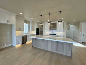 Kitchen with decorative light fixtures, light hardwood / wood-style flooring, dishwasher, a large island, and white cabinets
