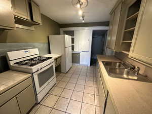 Kitchen featuring rail lighting, sink, light tile patterned floors, and white appliances