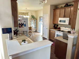 Kitchen featuring sink, white appliances, a textured ceiling, decorative light fixtures, and a chandelier