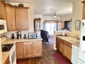 Kitchen with sink, white appliances, dark wood-type flooring, and ceiling fan